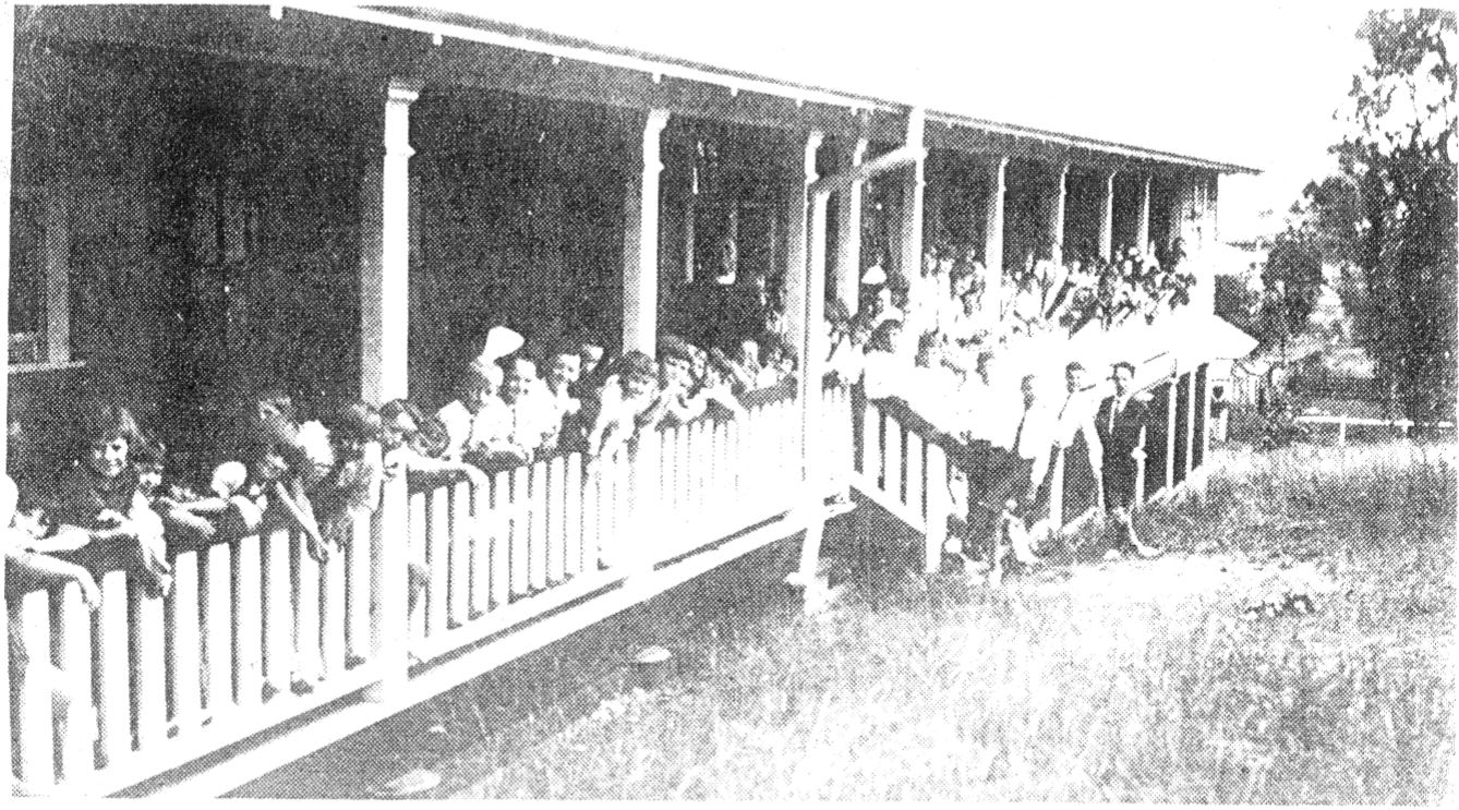 Historic photograph of students and staff gathered along a verandah at an early school building, reflecting the beginnings of the school community and its long‑standing tradition of learning and connection