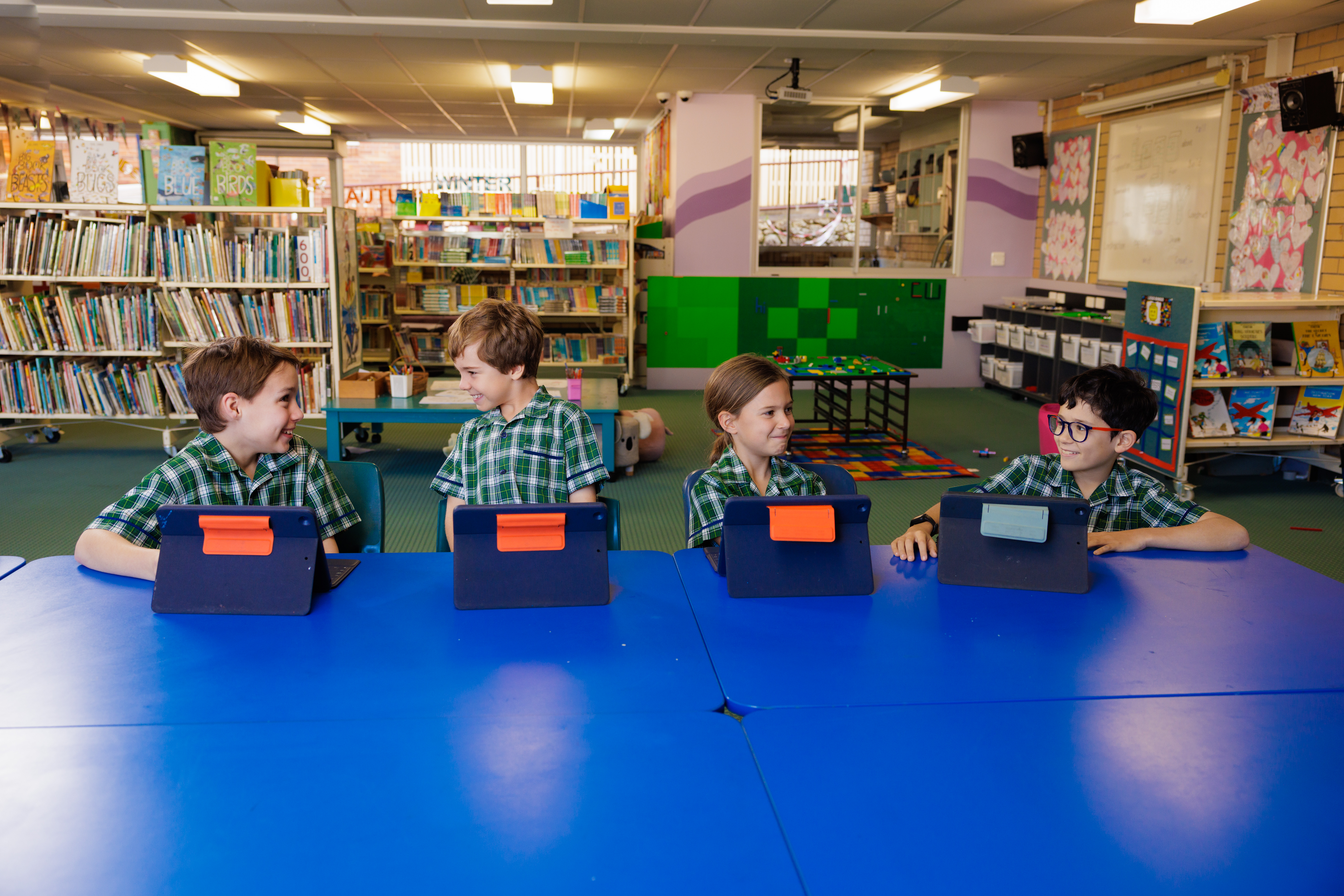 Students using tablets together in a library learning space, highlighting collaborative learning, digital engagement and a supportive primary school environment