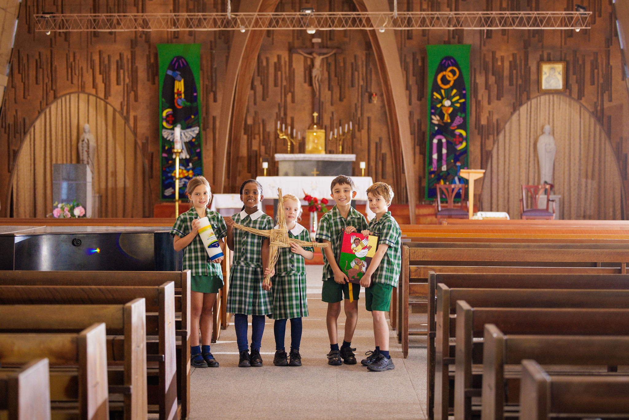 Students gathered inside a church holding faith symbols, highlighting shared worship, Catholic identity and spiritual learning within the school community
